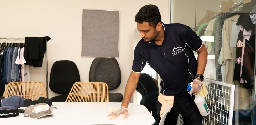 Urban Clean cleaner wiping down a table in a retail showroom fitting room.