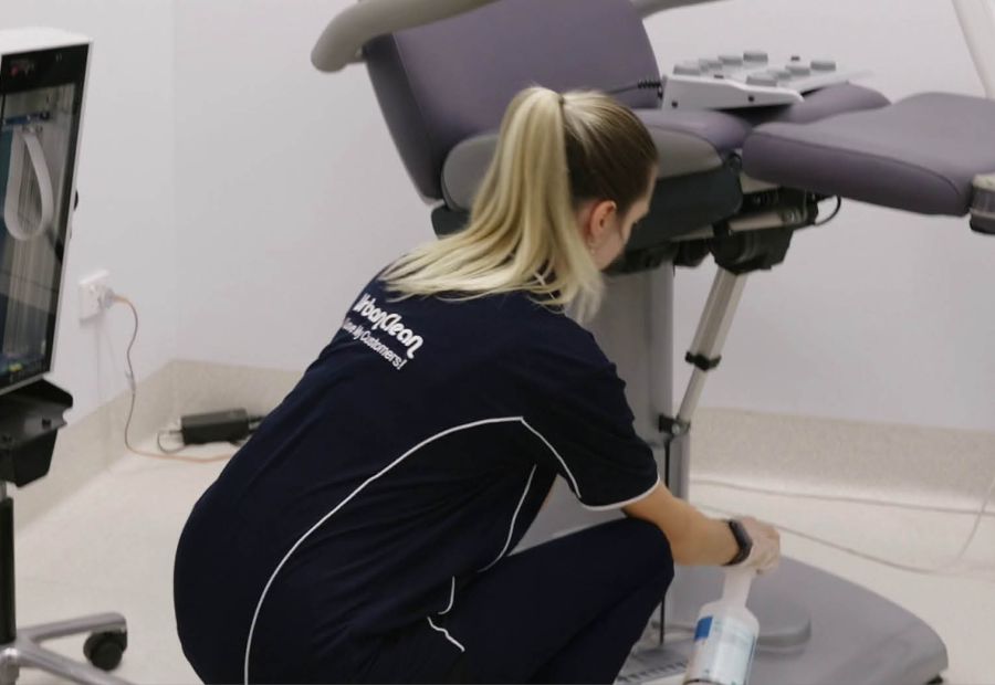 Urban Clean cleaner disinfecting a treatment chair inside a medical clinic room.