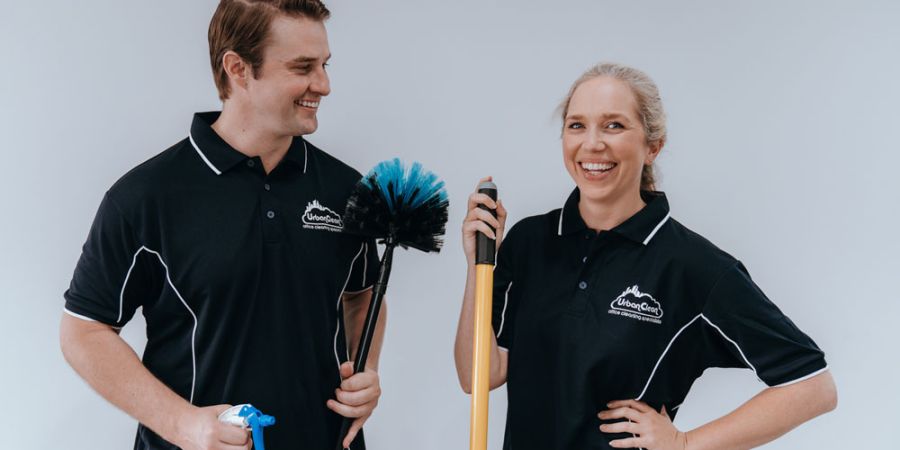 Two smiling Urban Clean staff members pose with cleaning tools in a studio portrait.